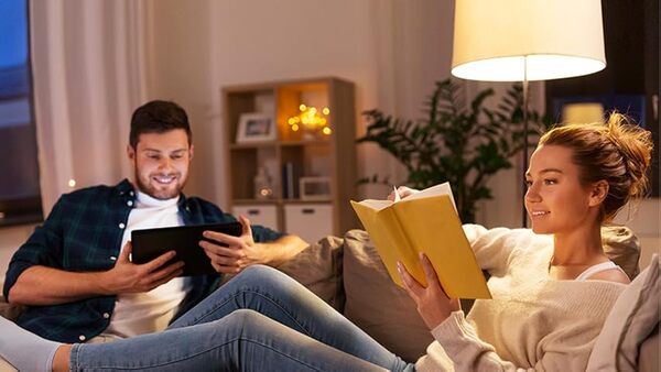 Person relaxing on a sofa with a book and warm light in the evening